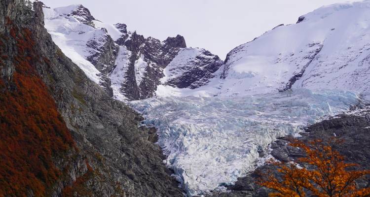 Gletsjer omringd door rotsachtige bergen met wat herfstkleuren.