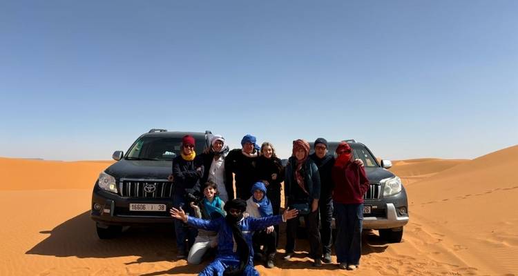 Groupe de personnes posant avec des SUV dans le désert.