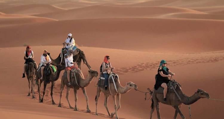 Mensen die op kamelen rijden in een woestijn met zandduinen.