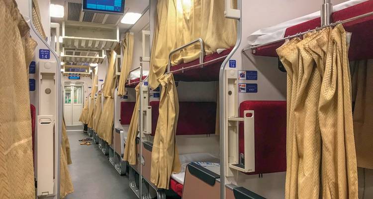 Intérieur d'un train avec des couchettes aménagées et des rideaux fermés.