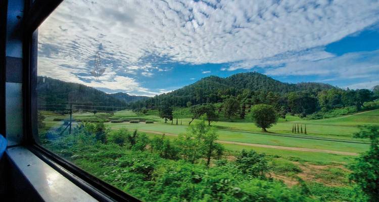 Vue panoramique depuis la fenêtre d'un train montrant des montagnes et un ciel bleu.