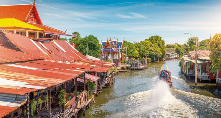 Lebendige Kanalszene mit einem Boot und traditionellen Häusern in Thailand.