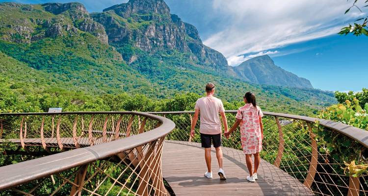 Couple marchant sur une promenade en planches avec des montagnes en arrière-plan.