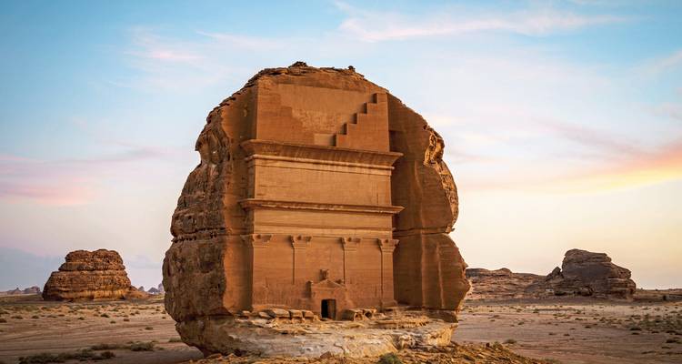Tumba antigua excavada en roca con un paisaje desértico durante el atardecer.