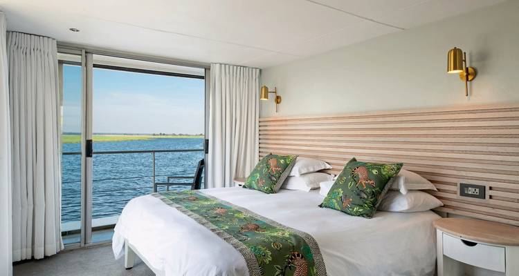 Luxurious bedroom with a view of a calm river through large windows.