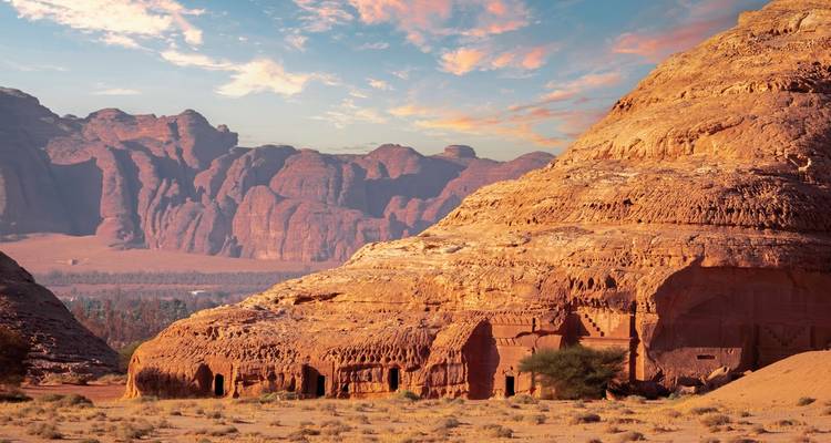 Desert landscape with rock formations and archeological site at sunset.