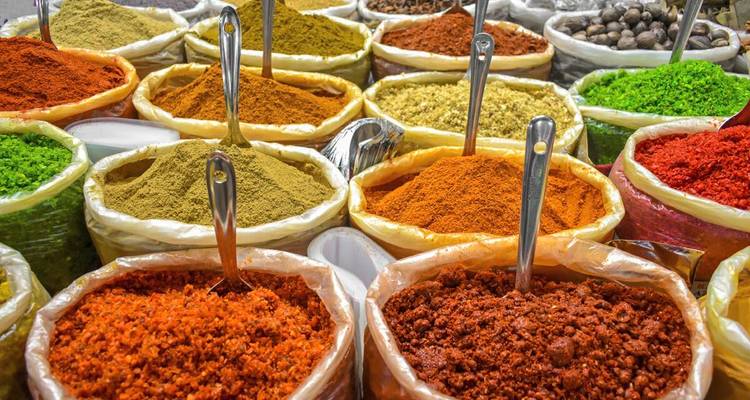 Colourful mounds of ground spices fill open sacks at a bustling market stall.
