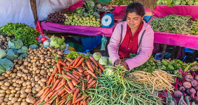 A vendor arranges fresh vegetables and fruits at a vibrant outdoor market stand.