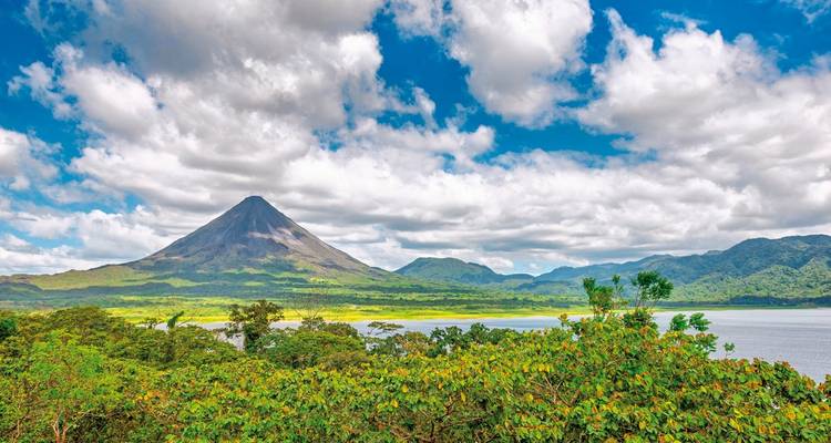 Arenal Volcano with lush green forest and a blue sky.