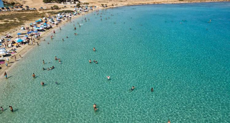 Baie d'un turquoise cristallin remplie de baigneurs le long d'une plage de sable fin bordée de parasols.