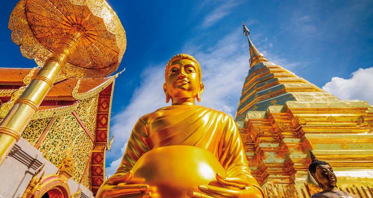Statue dorée de Bouddha dans un temple sous un ciel bleu.