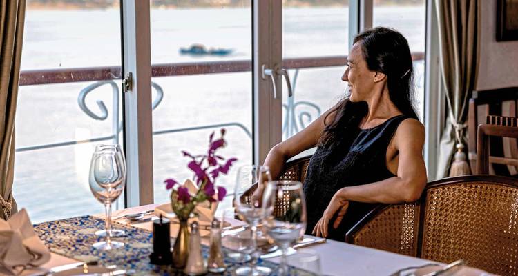 Frau, die an einem Tisch in einem Essbereich mit Flussblick sitzt.