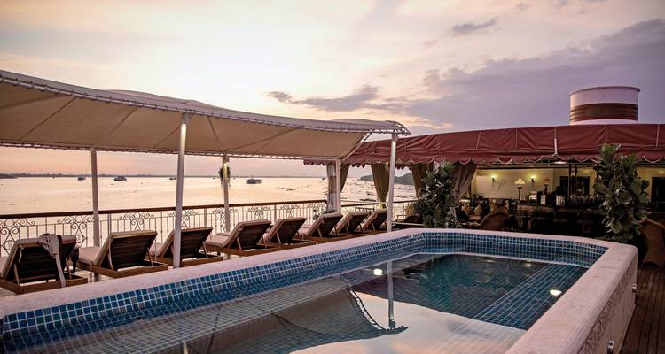 Pooldeck auf einem Kreuzfahrtschiff bei Sonnenuntergang mit Liegestühlen.