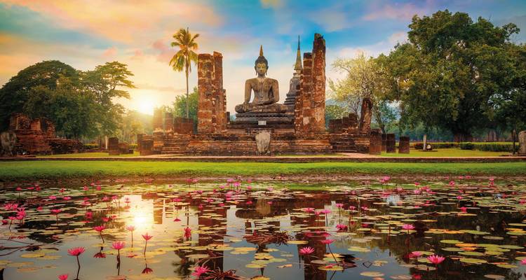 Buddha statue with a pond and lilies at sunset.