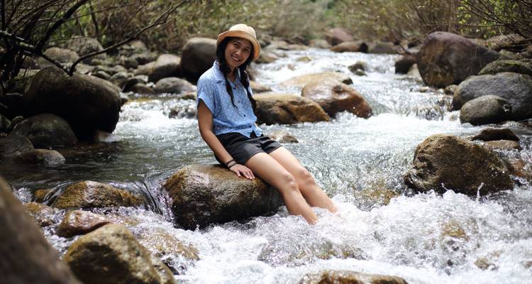 Girl sitting on a rock with her feet in a flowing stream.