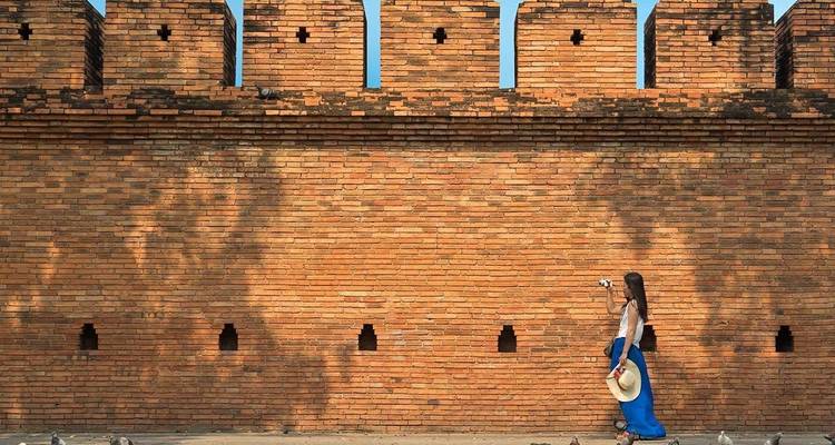 Een persoon die langs een oude bakstenen muur loopt, mogelijk een historische locatie.