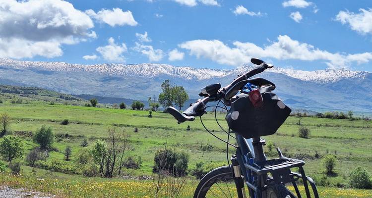 Una bicicleta estacionada al lado de un prado verde con montañas con franjas de nieve bajo un cielo azul brillante.