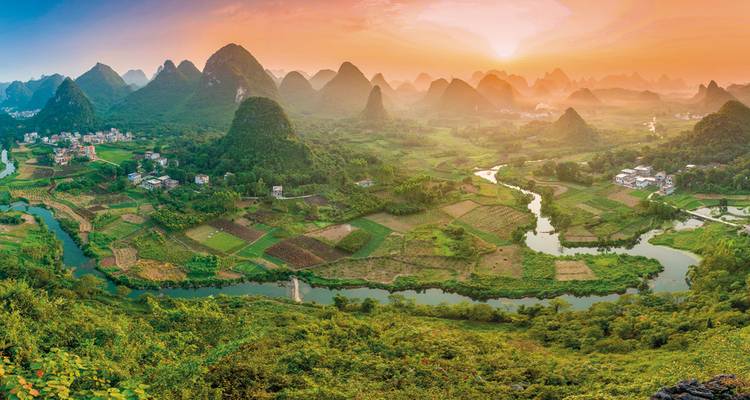 Una vista panorámica de exuberantes valles verdes con ríos y montañas kársticas al atardecer.