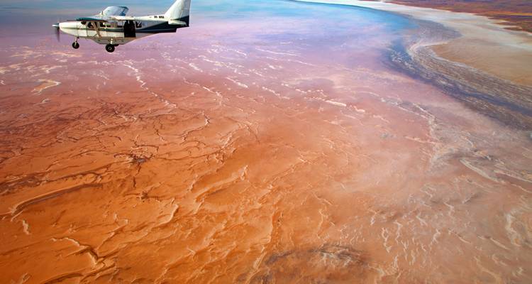 Kleines Flugzeug fliegt über eine weite Wüstenlandschaft.