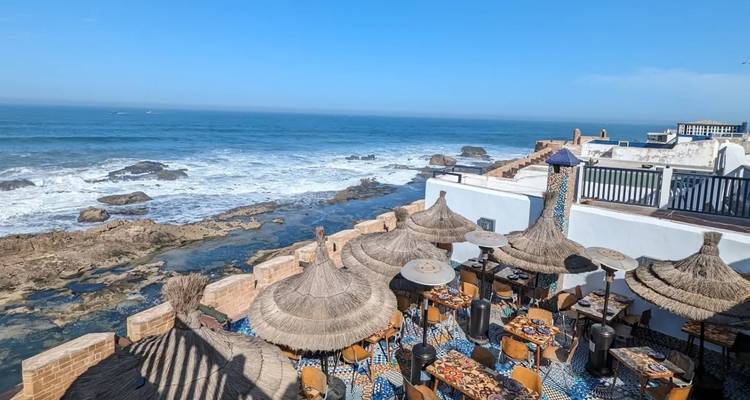 Zeezicht vanaf een terras met gevlochten parasols en meubels.
