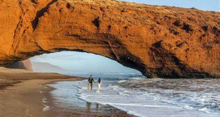 Een koppel dat wandelt op een strand met een natuurlijke boog bij Legzira.