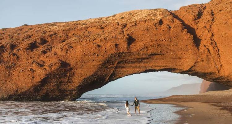 Een koppel dat wandelt op een strand met een natuurlijke boog bij Legzira.