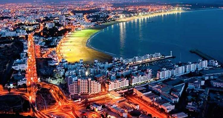 Nachtbeeld van een kuststad met verlichte gebouwen en een strand.