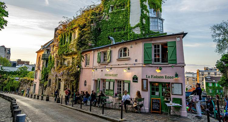 El encantador café La Maison Rose cubierto de hiedra en una esquina de adoquines en Montmartre al atardecer.