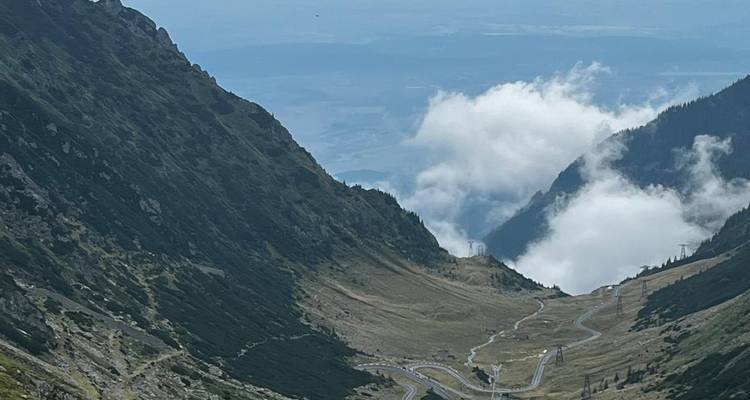 Serpenteante carretera alpina Transfagarasan zigzagueando a través del empinado valle montañoso de los Cárpatos parcialmente velado por nubes.