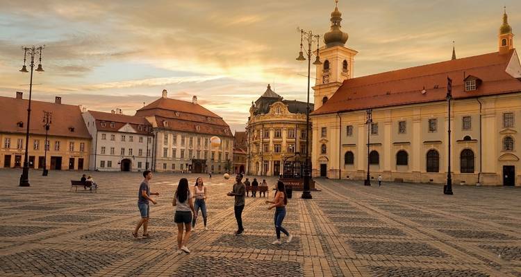 Amigos charlando en la gran plaza barroca de Sibiu al atardecer dorado.