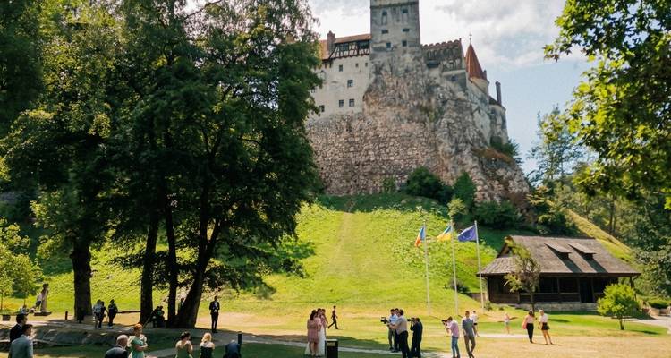 Les visiteurs se rassemblent sur la pente herbeuse sous l'imposant château de Bran juché au sommet d'une colline rocheuse.