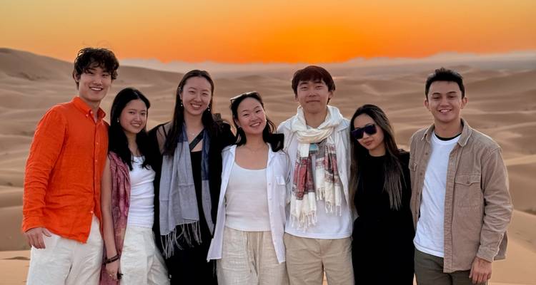 Een groepsfoto van mensen in de woestijn met een zonsondergang op de achtergrond.