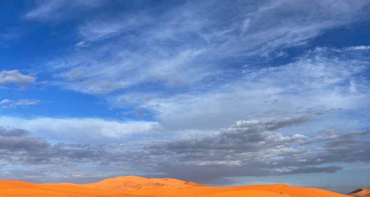 Uitgestrekt woestijnlandschap met duinen en een blauwe hemel vol wolken.