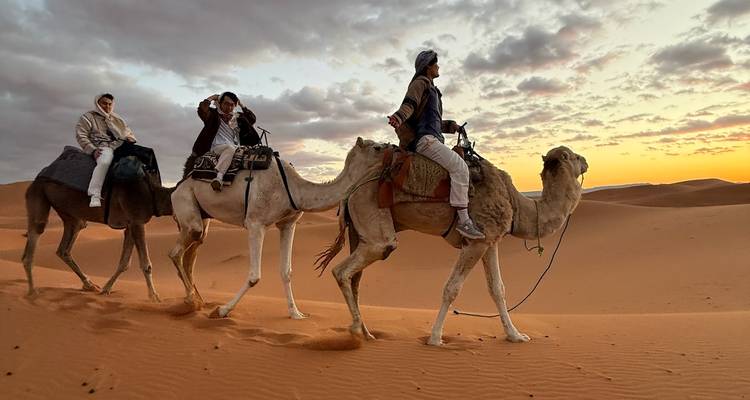 Mensen die op kamelen door de woestijn rijden met een prachtige zonsondergang.