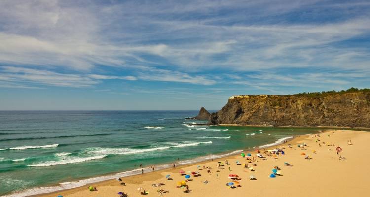 Scène de plage avec des gens qui prennent un bain de soleil et une falaise rocheuse en arrière-plan.