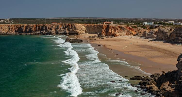 Plage ouverte avec des vagues de surf et des falaises qui entourent la zone.