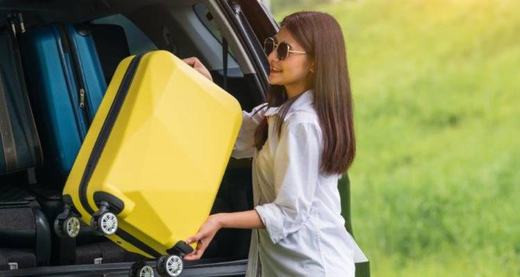 Woman loading a yellow suitcase into the back of a vehicle.
