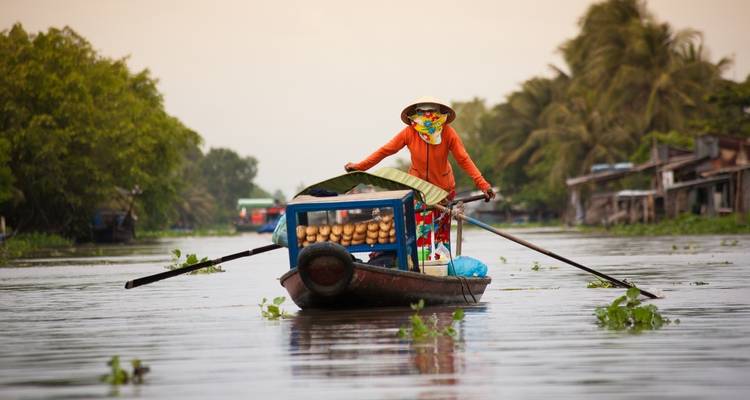 Een vrouw die goederen verkoopt op een boot in een landelijke rivieromgeving.