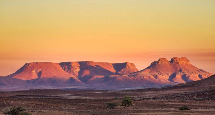 Les montagnes isolées aux sommets plats rougeoient de teintes roses au coucher du soleil au-dessus des plaines arides du Damaraland.