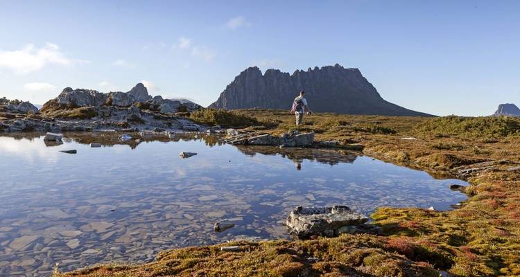 Wanderer, der an einem See steht, mit Bergen im Hintergrund.