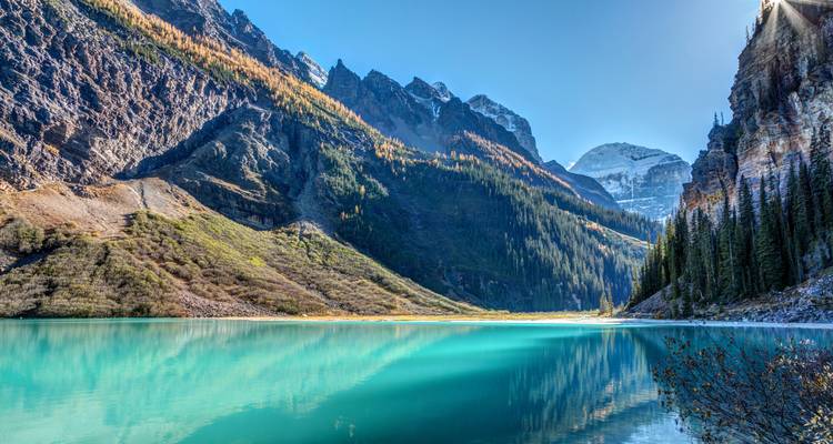 Atemberaubende Aussicht auf den Lake Louise mit umliegenden Bergen und klarem Wasser, das den Himmel widerspiegelt.