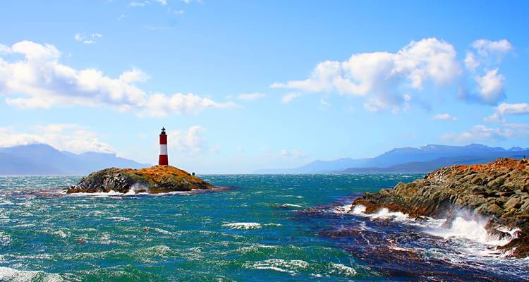 Een vuurtoren op een rotsachtig eiland met de oceaan eromheen.