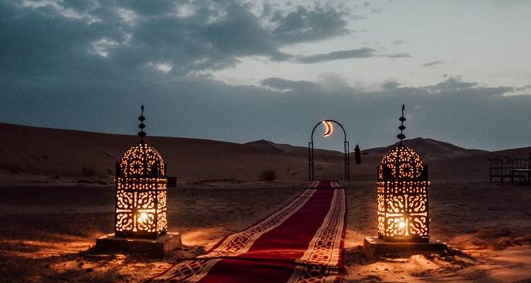 Lanternes décoratives et tapis rouge menant dans le désert au crépuscule.