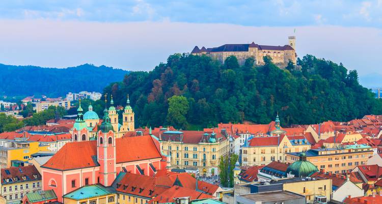Ljubljana’s red-roofed old town with hilltop castle surrounded by forested mountains.