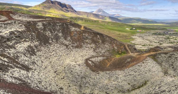 Paysage de cratère volcanique expansif avec une végétation en patchwork et des pics pyramidaux au loin.