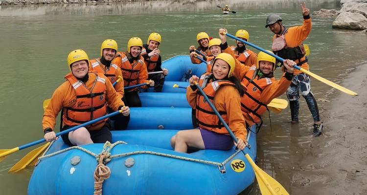 Grupo sonriente de remeros en bote inflable azul posando con remos en la orilla de un río nepalí