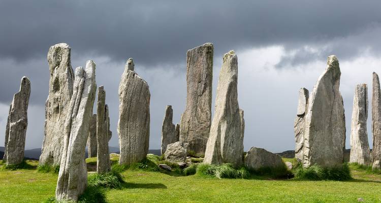 Anciennes pierres dressées de l'ensemble des Pierres Debout de Callanish se détachant contre un ciel gris dramatique et de l'herbe verte.