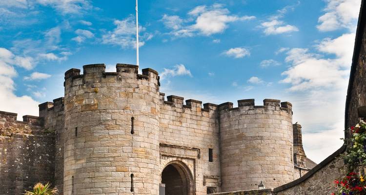 Portail de pierre et tours rondes du château de Stirling contre un ciel bleu vif avec des nuages épars.