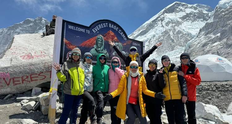Groep toeristen die poseren bij Everest Base Camp met besneeuwde bergtoppen op de achtergrond.