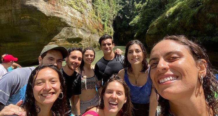 Un grupo de personas sonriendo para una selfie cerca de un cañón con vegetación exuberante.